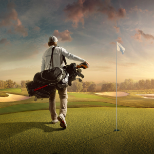 Golfer carrying a golf bag and walking toward the flag on the green at sunset