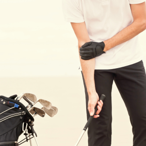 Golfer holding his elbow in pain next to a golf bag on the course