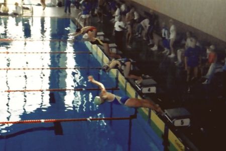 swimmers jumping in a pool from a starter block